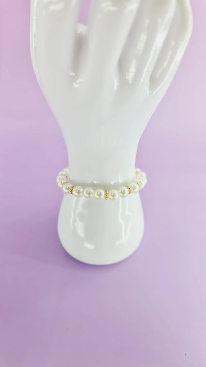 Bracelet perles blanches et dorées sur support, bijou tendance 974 Réunion, fond violet.