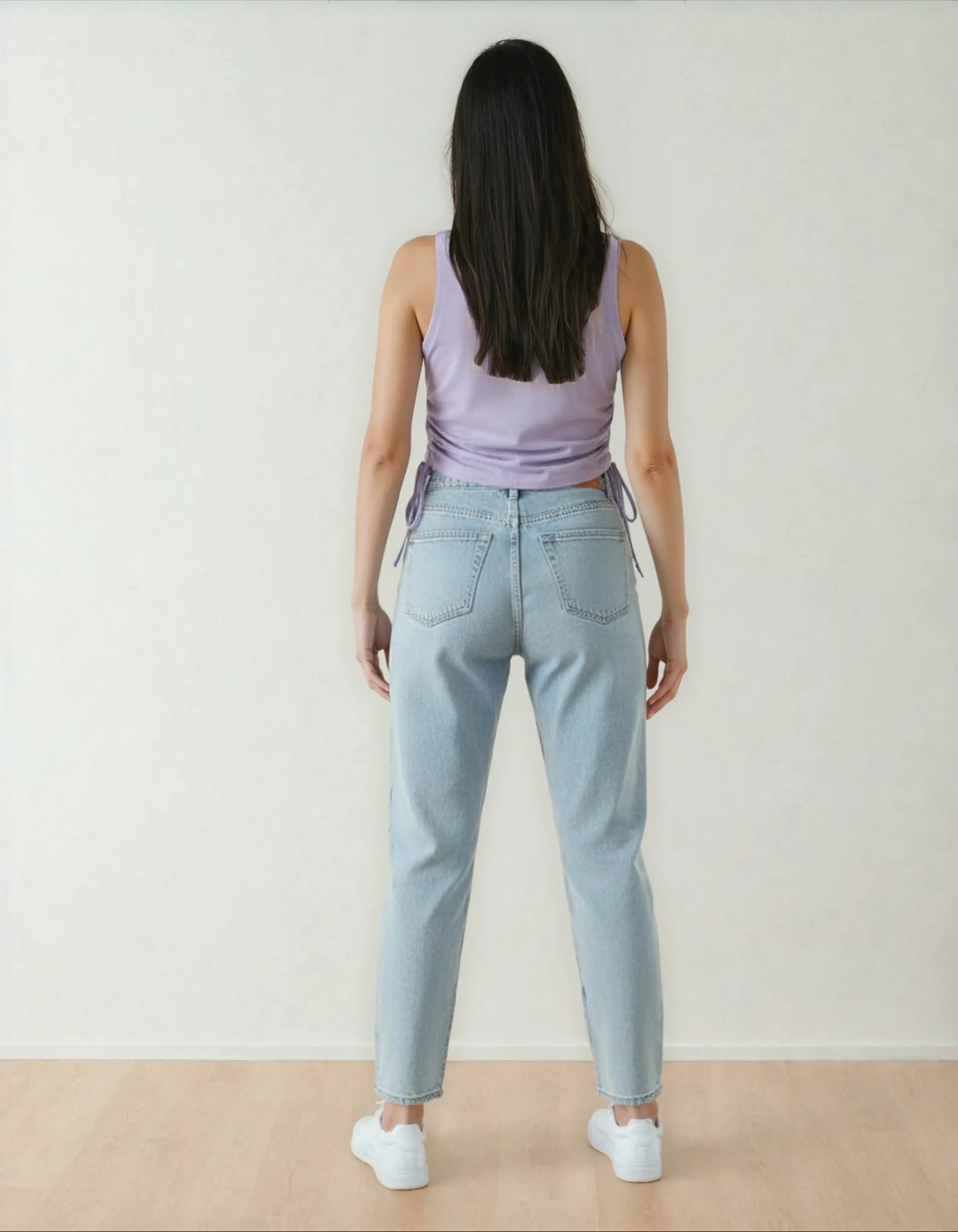 Femme de dos portant un jeans clair et un débardeur lavande, sol bois, 974 Réunion